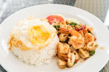 Yasemin pilavı ve kızarmış yumurta üzerine fesleğen yapraklı baharatlı deniz ürünleri.