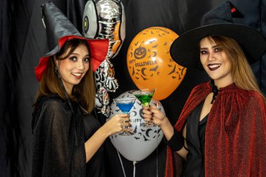 Two young adult and teenager girls celebrating a Halloween party carnival Festival in Halloween costumes drinking alcohol cocktail