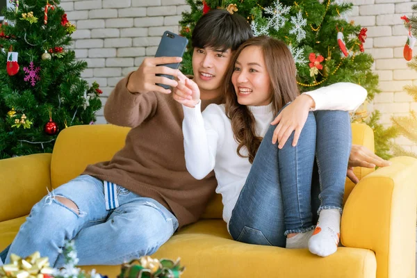 若いですアジアの大人のティーンカップルは一緒にクリスマスツリーの装飾とリビングルームで一緒にクリスマス休暇を祝うために写真を撮ります — ストック写真