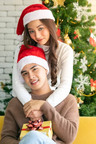 若いですアジアの大人のティーンカップル保持ギフトプレゼントボックス抱擁と一緒にクリスマスの休日を祝うクリスマスツリーの装飾とリビングルーム — ストック写真