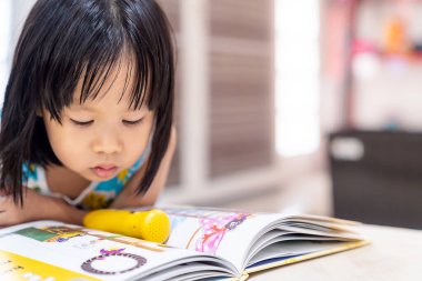 Asyalı kız çocuk, dünya çapında covid-19 salgını yüzünden şehir tecrit altındayken evdeki oturma odasında interaktif kitap okuyor. Home Schelling okul öncesi konsept için hazırlan.