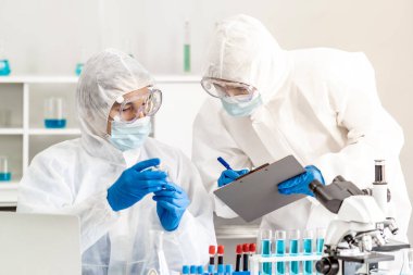 Bilim adamı, bilim laboratuarında Coronavirus covid-19 salgınının aşı testini inceliyor. Bilim adamları PPE kişisel koruyucu giysiler ve tıbbi gözlük takıyor. Tıp bilimi teknolojisi ve sağlık hizmeti kavramı.