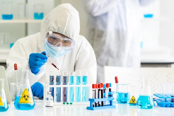 Bilim insanları, Coronavirus covid-19 aşısını araştırmak ve geliştirmek için tüp rafta bulunan tüpte kan numunesi bırakmak için kan damlatıcıyı kullanıyor. Tıp Bilimi konsepti.