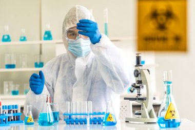 Bilim adamları deney tüpünü tutuyor ve Coronavirus covid-19 aşısı için laboratuvar odasında ihtiyatlı işaretlerle aşı geliştiriyor. Tıp bilimi ve teknoloji konsepti.