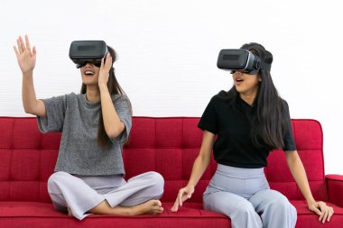 İki Asyalı güzel kadın, video oyunları oynarken gülümsüyor. Oturma odasında iyi bir ruh sağlığı için karantina altında. Oyun teknolojisi eğlence ve ruh sağlığı konsepti.