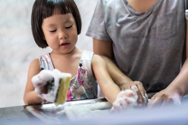 Asyalı kız annesiyle bulaşık ve sofra takımı yıkıyor, çocuk için ev işi çocuk için yönetici görevi yapıyor. Çocuk yaşam tarzı ve aile konsepti için ev işi. 