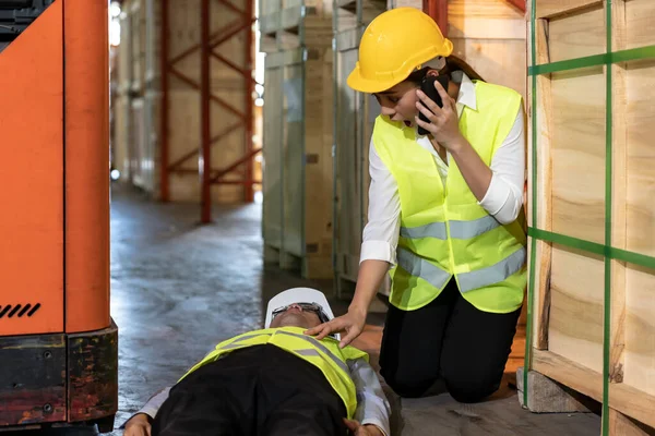 Asian worker Call an ambulance after warehouse manager lying down on warehouse floor after accident from forklift. Using for safety first and business insurance concept.