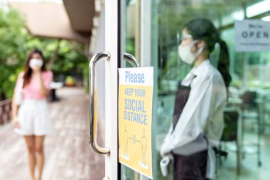 Asyalı garsonun arka planda müşteriyi karşılamaya hazır olduğu yeni normal restoran için sosyal mesafe tabelası. Yeni normal restoran yaşam tarzı konsepti.