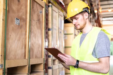 Beyaz Kafkasyalı bir depo çalışanı büyük bir depo dağıtım merkezinde envanter kontrolü için dijital tablet kullanıyor. İşletme deposu teknolojisi ve lojistik konsepti yeniden açılıyor