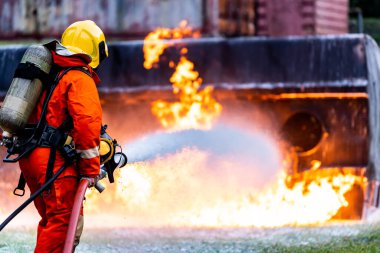 İtfaiyeci, petrol tankeri kazasındaki yangın aleviyle savaşmak için kimyasal köpük yangın söndürücü kullanıyor. İtfaiyeci güvenlik kazası ve kamu hizmeti konsepti.