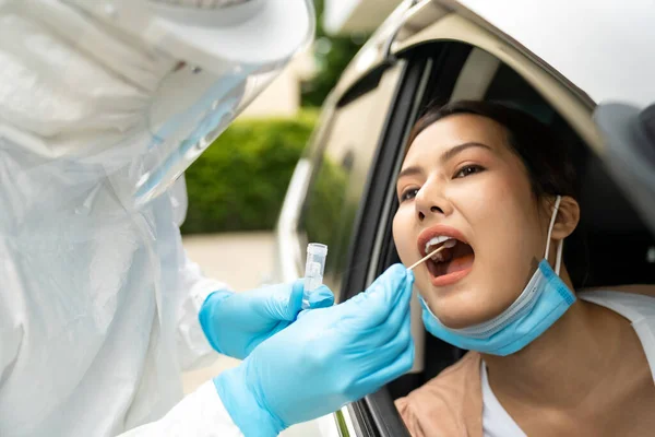 Portrait of Asian woman drive thru coronavirus covid-19 test by medical staff with PPE suit by throat swab. New normal healthcare drive thru service and medical concept.