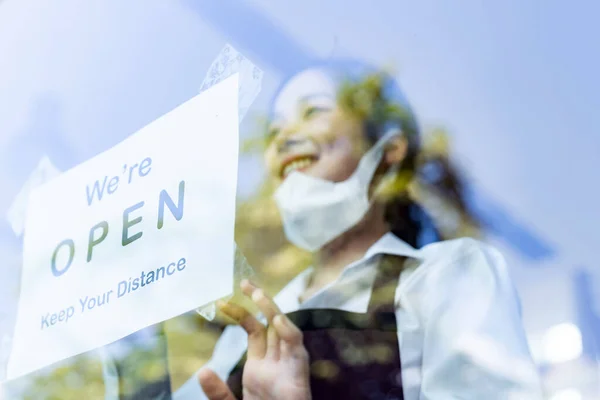 Focus on restaurant signage. Asian female waitress putting on open signage with social distance for new normal restaurant. New normal restaurant lifestyle concept.