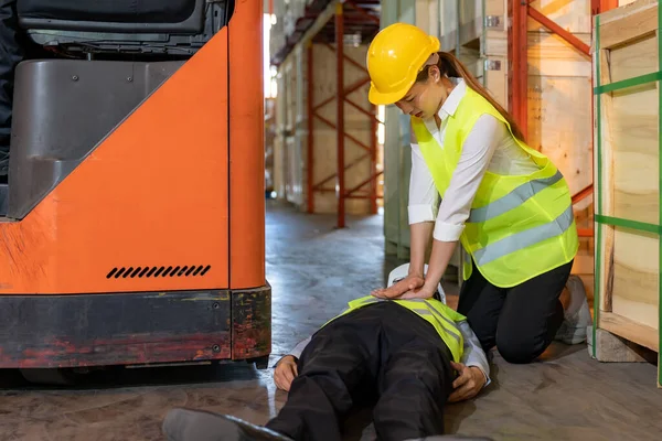 Asian worker do Cardiopulmonary Resuscitation CPR after warehouse manager lying down on warehouse floor after accident from forklift. Using for safety first and business insurance concept.