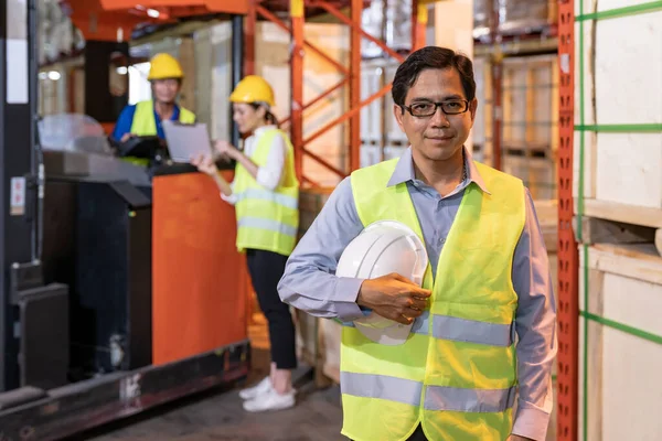 アジアの倉庫管理者の肖像は 倉庫労働者とハード帽子を保持するバックグラウンドで在庫を確認するためにフォークリフトを動作します 倉庫技術 物流コンセプトの再オープン ロイヤリティフリーのストック写真