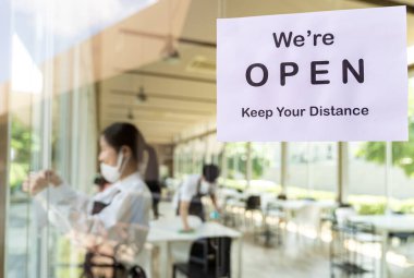 Restoran tabelasını yeni normal bir restoran için sosyal mesafeyle yeniden açarken Asyalı garson ve garsonun geçmişi açılıştan önce restoranı hazırlıyor. Yeni normal restoran yaşam tarzı konsepti.