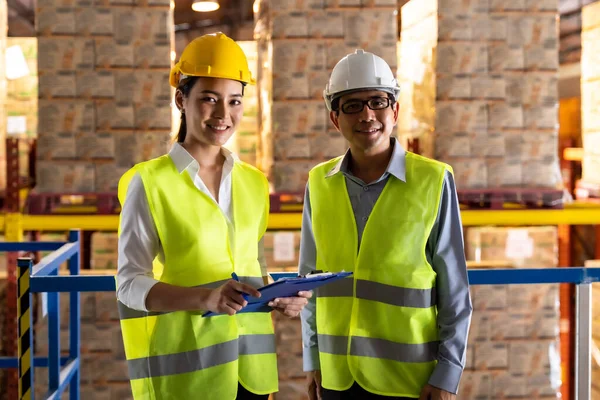 Portrait of asian warehouse manager and warehouse worker with clipboard to assign job with distribution warehouse in background. Reopening business warehouse technology and logistic concept.