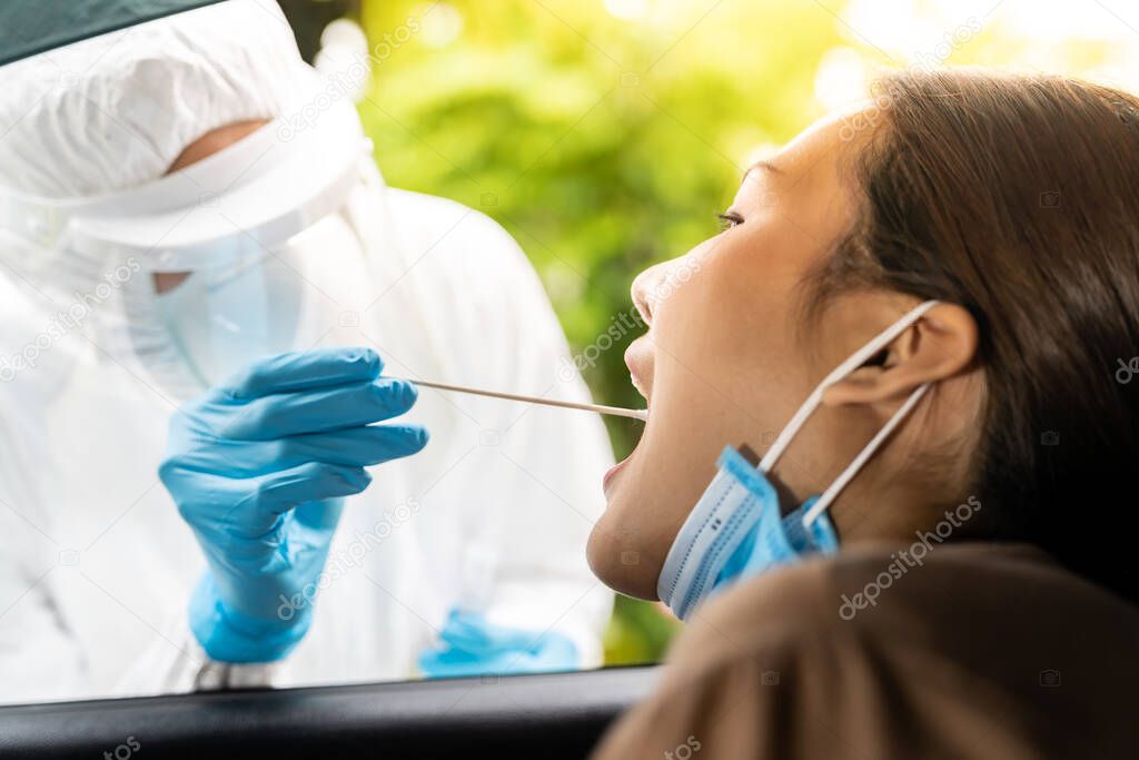 Portrait of asian woman drive thru coronavirus covid-19 test by medical staff with PPE suit by throat swab. New normal healthcare drive thru service and medical concept.