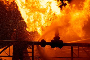 Firefighter using water fog type fire extinguisher to fighting with the fire flame from oil pipeline leak and explosion on oil rig and natural gas station. Firefighter and industrial safety concept. clipart