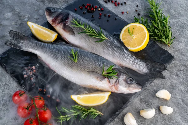 新鲜的生鲈鱼 柠檬番茄和香料在黑色石板上 冰霜冷蒸汽雾 市面新鲜食品海产食品概念 — 图库照片