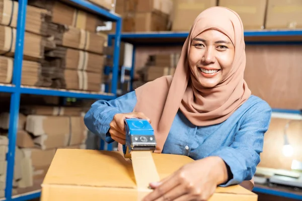 Portrait of Islam Muslim female asian warehouse worker packing and labelling on cardboard box in warehouse environment. Using in business warehouse logistic concept.