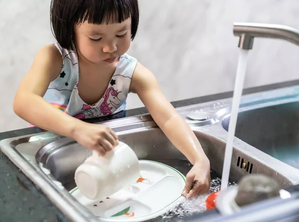 Asian girl washing her dish and tableware by herself, housework for child make executive function for kid. House-working for kid lifestyle and family concept.