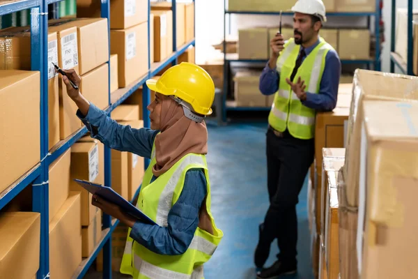 Islam Muslim female warehouse worker do logistic inventory route with his manager use walky talky inbackground in warehouse distribution. For business warehouse inventory and logistic concept.