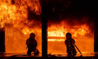 İtfaiyeciler büyük binadaki yangın aleviyle savaşmak için yangın söndürücüyü kullanıyorlar. İtfaiyeci ve endüstriyel güvenlik felaketi ve kamu hizmeti kavramı.