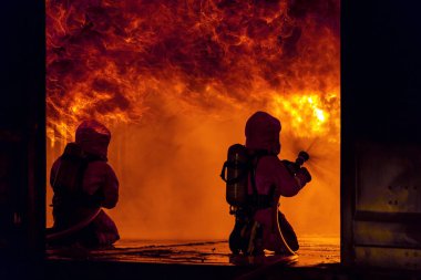 İtfaiyeciler büyük binadaki yangın aleviyle savaşmak için yangın söndürücüyü kullanıyorlar. İtfaiyeci ve endüstriyel güvenlik felaketi ve kamu hizmeti kavramı.