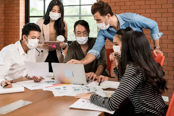 Group of asian and caucasian business person team meeting and brainstorm in meeting room after office reopen, they wear protective face mask as new normal practice to prevent coronavirus infection.