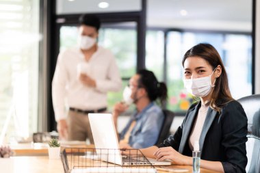 Asyalı ofis çalışanı iş kadını portresi, sosyal mesafe uygulaması Coronavirus COVID-19 'u engellediği için ırklar arası meslektaş ile normal ofiste koruyucu yüz maskesi takıyor..