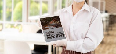 Panorama, yüz maskesi ve yüz kalkanı olan garsonu kapat. Müşteri için QR kodlu dijital tablet ile çevrimiçi temas kurulamayan menüleri tara. Bağlantısız ve yeni normal restoranlar için teknoloji konsepti.