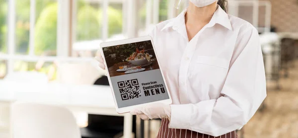 Panorama close up waitress with face mask and face shield hold digital tablet with QR code for customer to scan for online contactless menu Contactless and technology concept for new normal restaurant