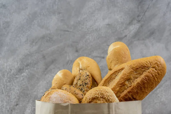 Variety bread in disposable paper bag on grey vintage loft background. Bakery food and drink and grocery concept for delivery.