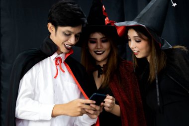 Group of friends asian young adult people see photo in mobile phone after take selfie photograph. They wear Halloween costume. Halloween celebrate and international holiday concept.