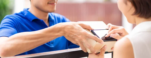 Panoramic Asian woman sign electronic signature to portable mobile device after receive packge from male delivery man in blue shirt. Package shopping delivery and digital sign concept.