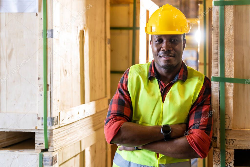 Portrait of african black warehouse worker standing and crossed his arms smile and looking at camera in large warehouse distribution center. Using in business warehouse and logistic concept.