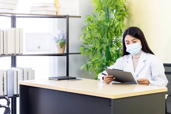 アジア女性医師の肖像画は 保護顔マスクを着用し 病院の診療所の彼女のオフィスルームに座って 忍耐を確認する前に忍耐ファイルを読んでください 新しいノーマルヘルスケアコンセプト — ストック写真