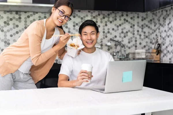 Asian couple work from home in the kitchen and eating delivery chinese take away food and take out coffee while city lockdown from coronavirus covid-19 pandemic. New Normal lifestyle working from home.
