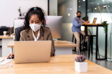 Afrikalı siyahi ve Asyalı iş kadınlarının melez ırkı, Coronavirus COVID-19 'un yayılmasını önlemek için yeni normal ofiste çalışan yüz maskesi takıyor.