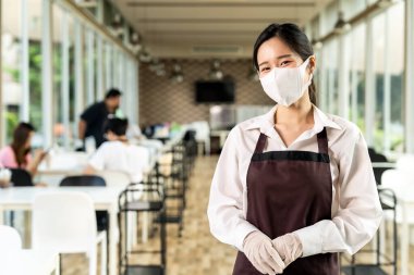 Çekici Asyalı garson kız, müşterilerinin geçmişine sahip yüz ifadesini takınıyor. Kapalı bir restoranda sosyal uzaklık masasında oturuyor. Yeni normal restoran yaşam tarzı konsepti.