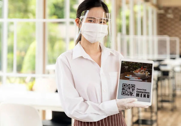 フェイスマスクとフェイスシールド付きアジアのウエイトレスは 顧客がオンライン非接触メニューをスキャンするためのQrコードを持つデジタルタブレットを保持しています 新しい通常のレストランのためのオンライン非接触と技術の概念 — ストック写真