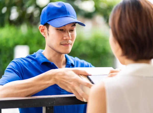 Asian woman sign electronic signature to portable mobile device after receive package from male delivery man in blue shirt. Package shopping delivery and digital sign concept.