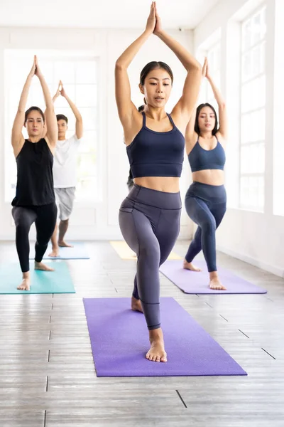 Group of young sporty attractive asian people practicing yoga lesson on Warrior and crescent pose with instructor coach in front in gym studio. Working out, fitness sport and healthy life concept.