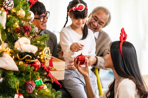 Multigenerational asian Family decorating a Christmas tree. Mom Dad daughter girl and grandfather decorate the Christmas tree prepare for season greeting of Merry Christmas and Happy Holidays.