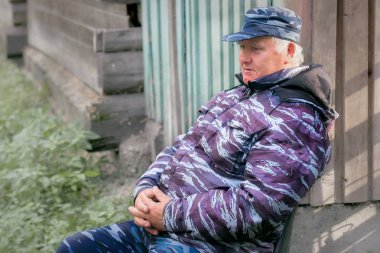 Kamuflaj giysili yaşlı bir adam açık havada bir sandalyede oturuyor. Emeklilik güvenlik görevlisi olarak iş kavramı.