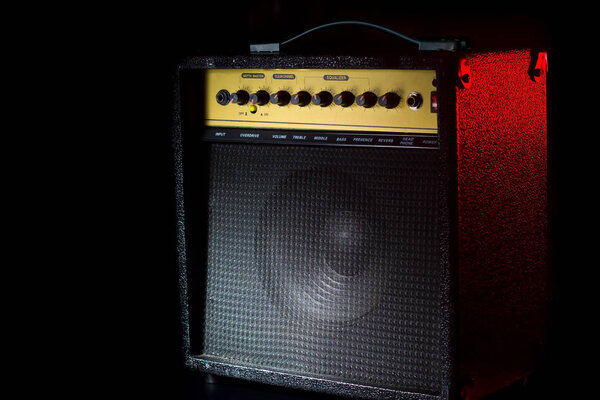 Black guitar amplifier on a black background with a red flash. Combo with lots of controls