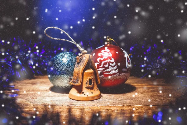 Christmas composition of Christmas decorations: two balls and a clay house. Studio photo with artificial snowflakes. The Central composition of the front view.