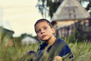 Serebral Palsili çocuk dalgın ve üzgün bakışı. Otların arasında oturan ve mesafe içine arıyorum yaz akşam çocuk.