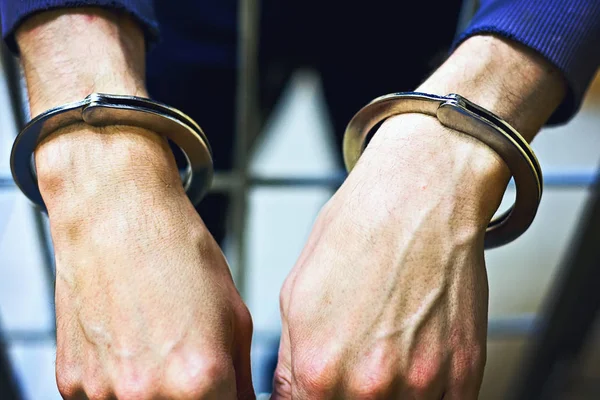 Manos masculinas con esposas de metal de cerca. Un prisionero en la cárcel. el concepto de castigo por un delito. imagen tonificada —  Fotos de Stock