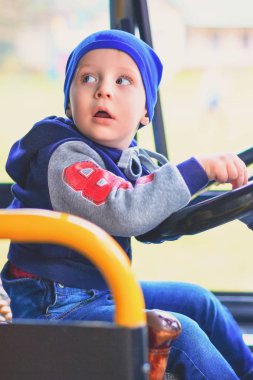 Küçük bir çocuk otobüsün direksiyonuna takside oturur ve geri görünüyor.